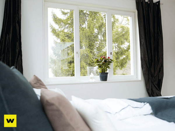 Helles Schlafzimmer mit großem Fenster, Blick ins Grüne und Pflanze auf Fensterbank.